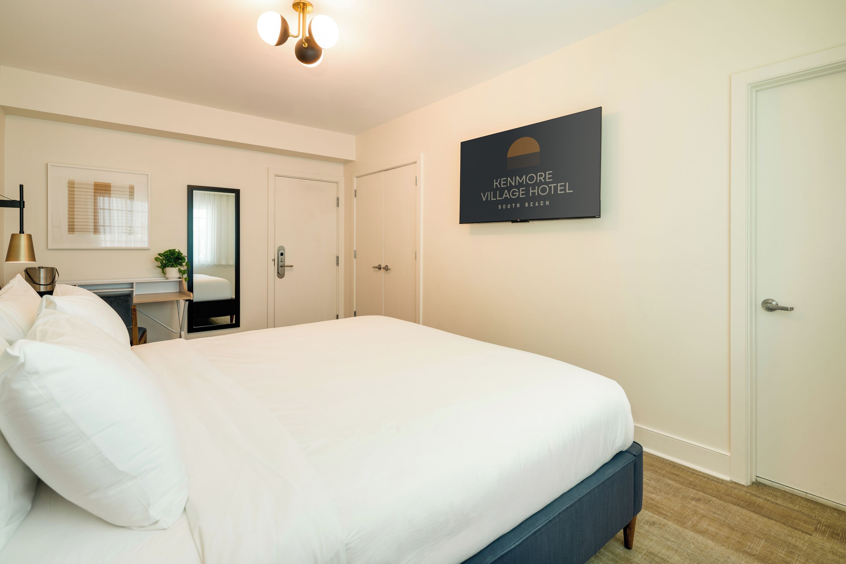 Une chambre d’hôtel avec un grand lit, un bureau avec une lampe, un miroir et un panneau encadré accroché au mur.