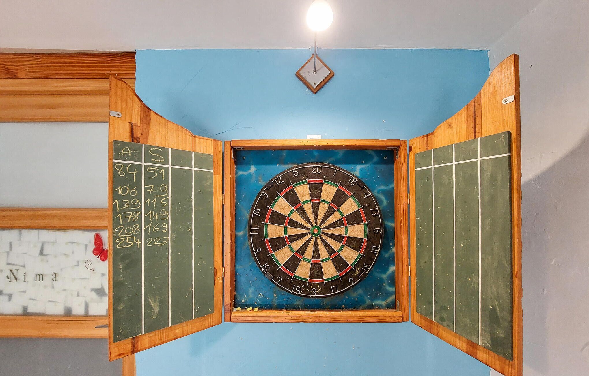 Un jeu de fléchettes fixé au mur, avec un tableau noir sur le côté gauche.