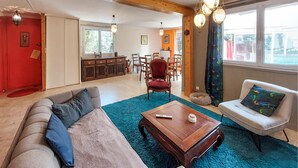 Un salon avec un canapé, une table basse et un fauteuil. Au fond, on aperçoit un coin repas avec une table et des chaises.