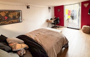 A bedroom with a bed, a desk, a chair, a map on the wall, and a view through a glass door.
