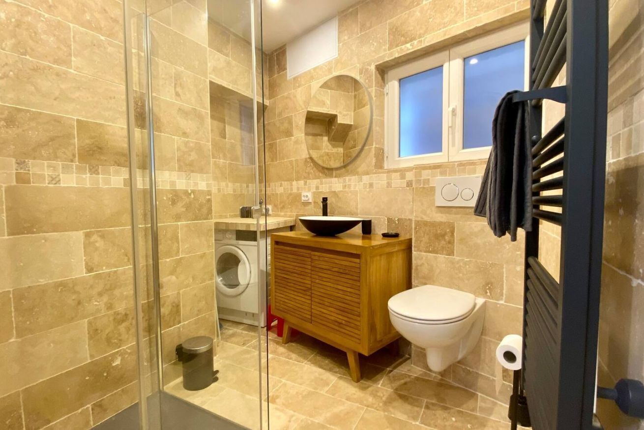 Un baño con cabina de ducha de vidrio, tocador de madera, inodoro y ventana.