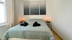 Un dormitorio con una cama, dos lámparas de noche, una ventana con cortinas y una pared decorada con tres cuadros.