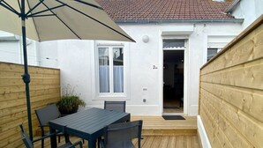Un patio con una mesa, sillas, una cerca de madera y una casa con techo de tejas.
