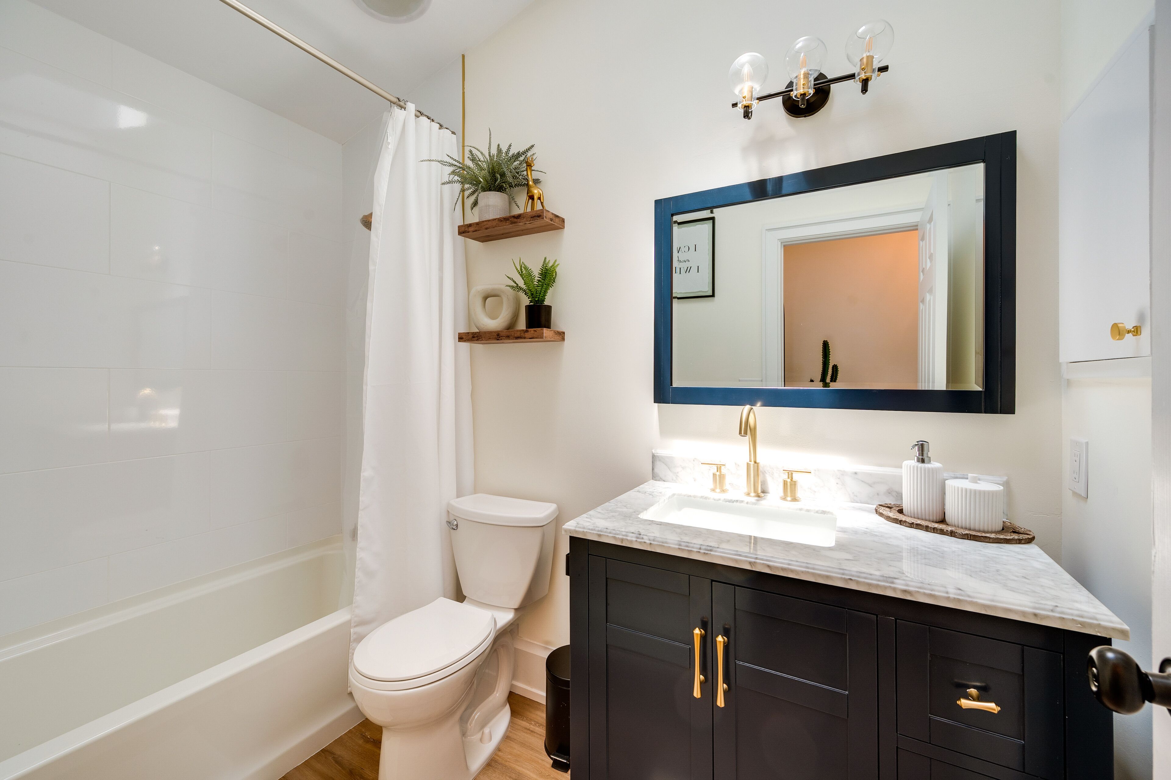 A modern bathroom with a white toilet, a shower, a large mirror, and a black vanity with gold handles.