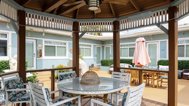 A covered outdoor patio with a round glass table and white chairs with floral upholstery. - Tropic Isle Boutique Hotel  (Hollywood)