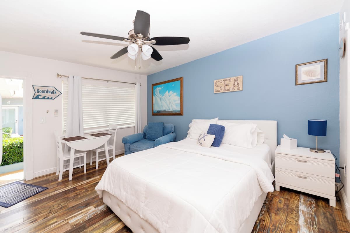 Quarto com cama, escrivaninha, cadeira, mesa de cabeceira e ventilador de teto.