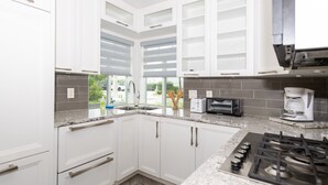 A modern kitchen with white cabinets, a granite countertop, a built-in oven, a coffee maker, and a window with a view of greenery. - Tropic Isle Boutique Hotel  (Hollywood)