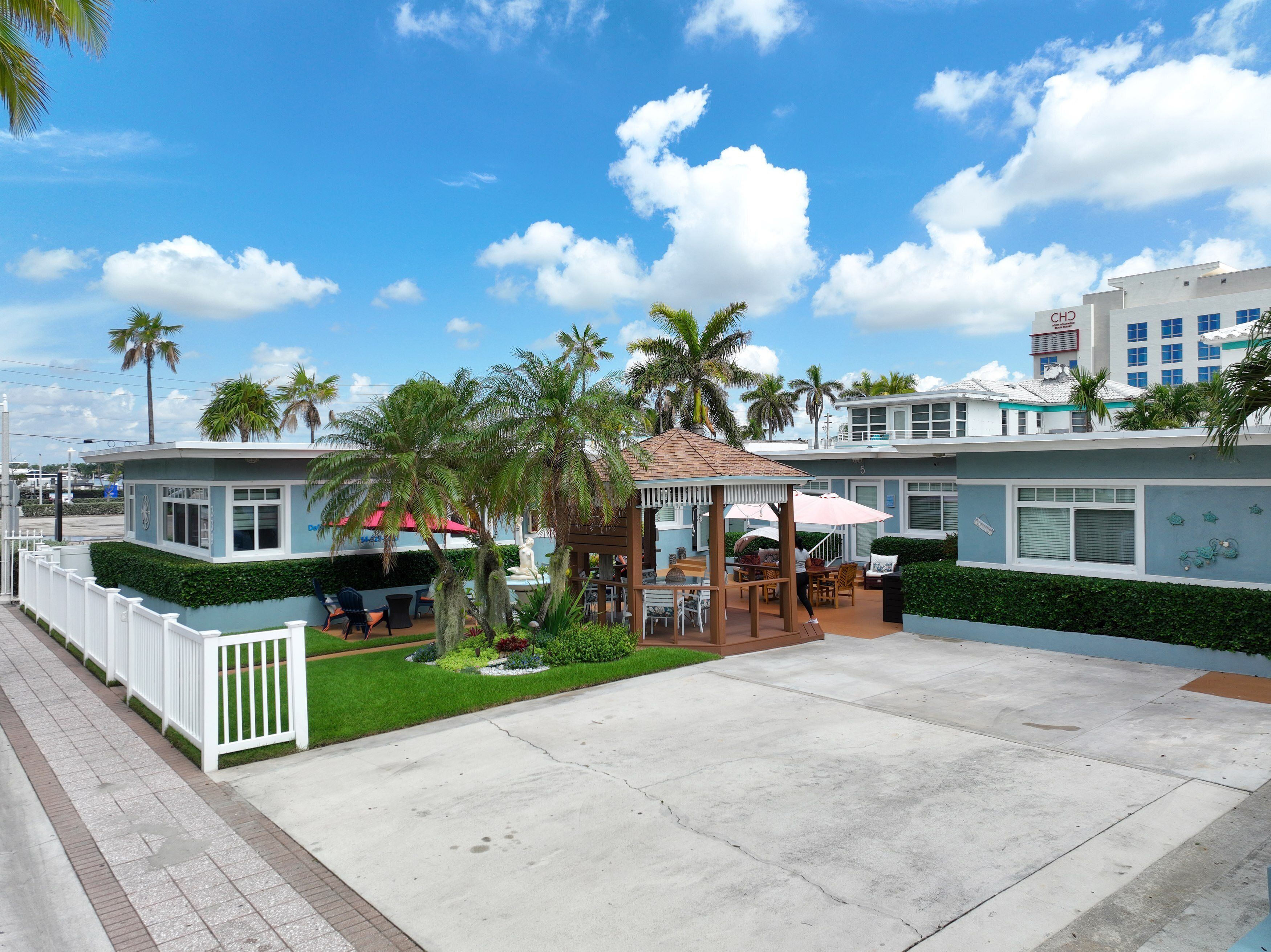 A hotel with a covered patio area, palm trees, and a clear blue sky.
