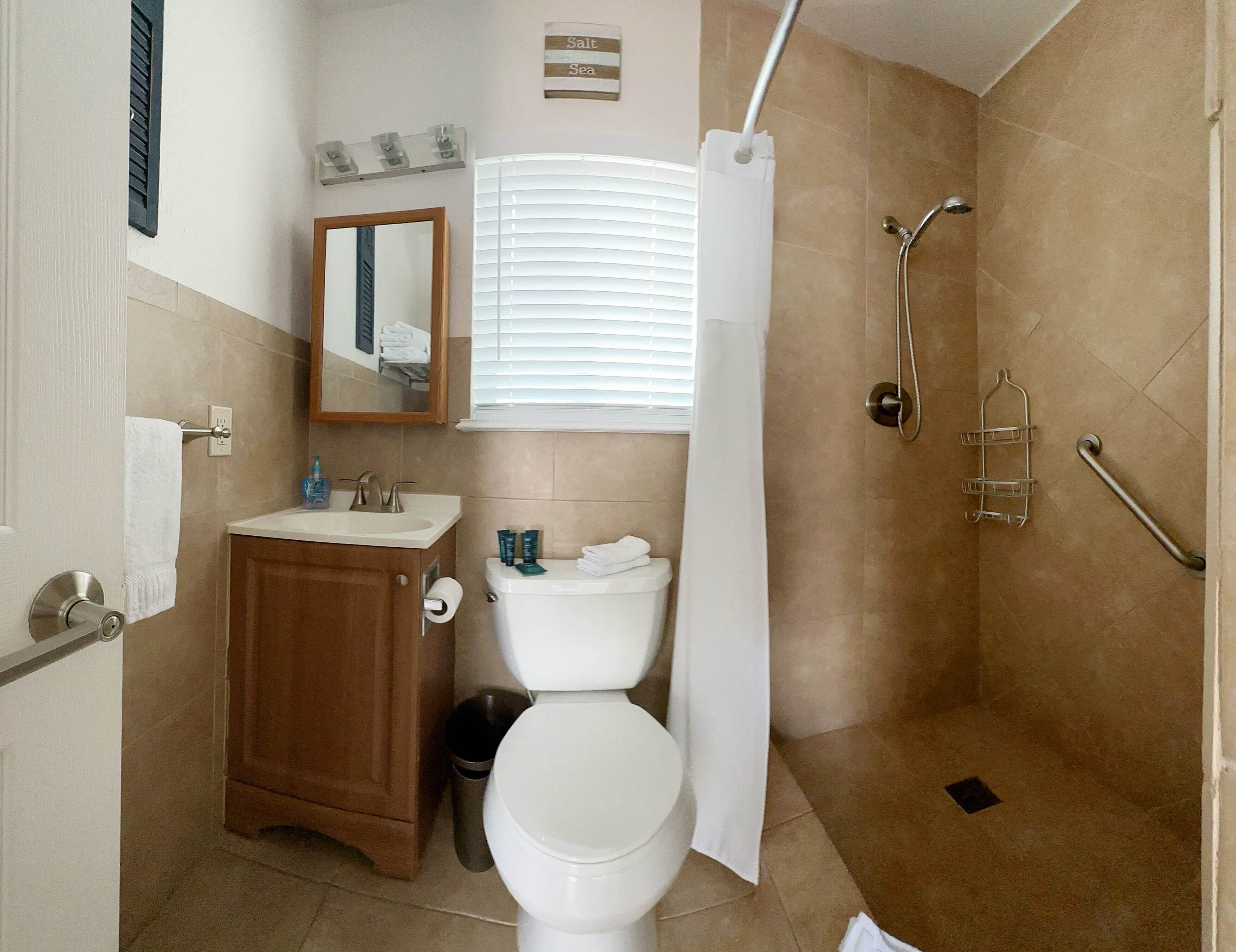 A bathroom with a toilet, sink, mirror, shower, and a towel rack.