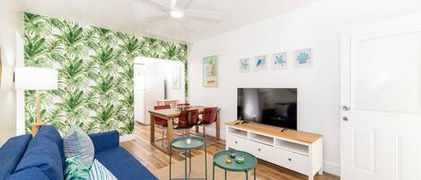 A modern living room with a blue sofa, a dining table, and a TV.