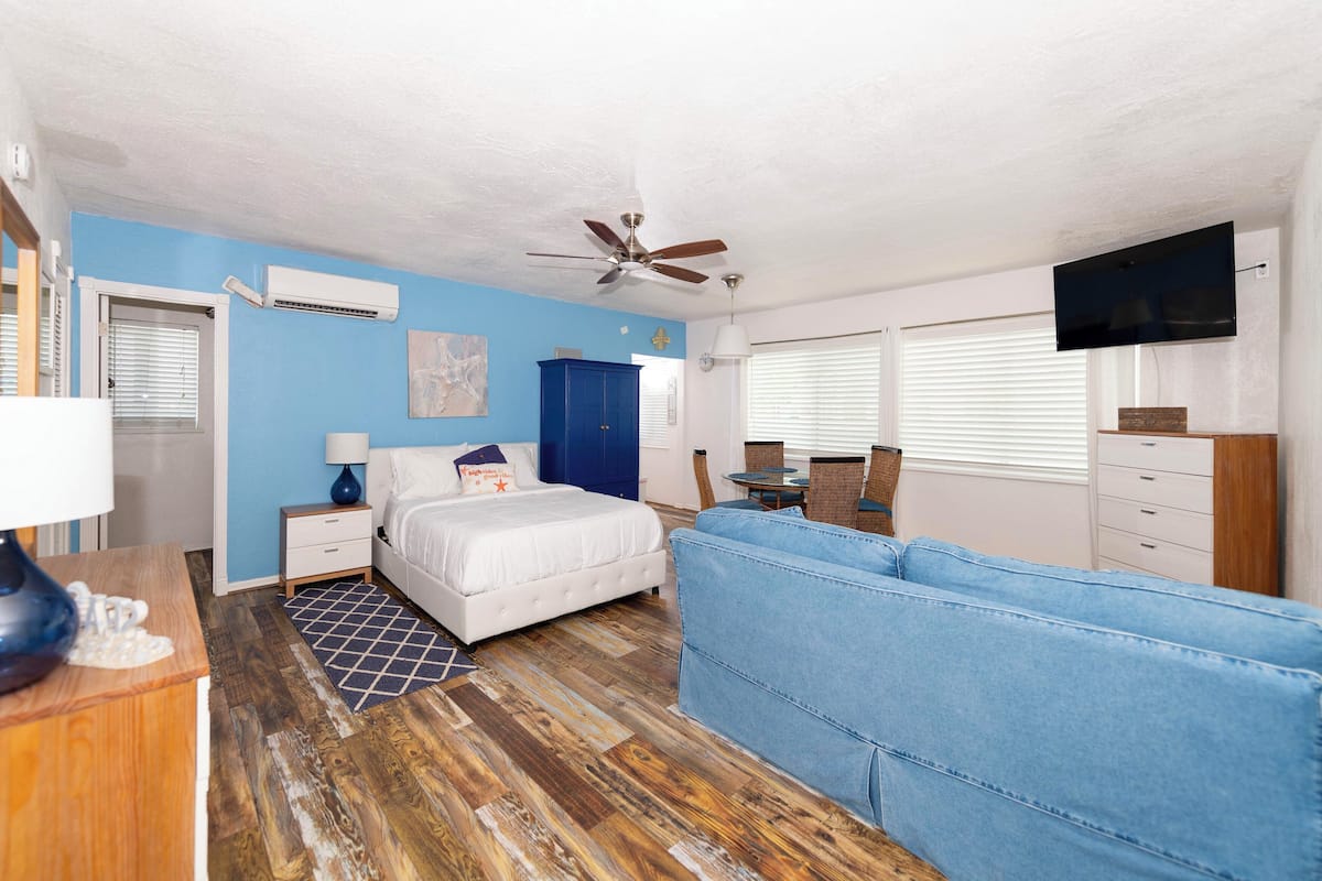Quarto com cama, sofá azul, ventilador de teto, televisão e guarda-roupa.