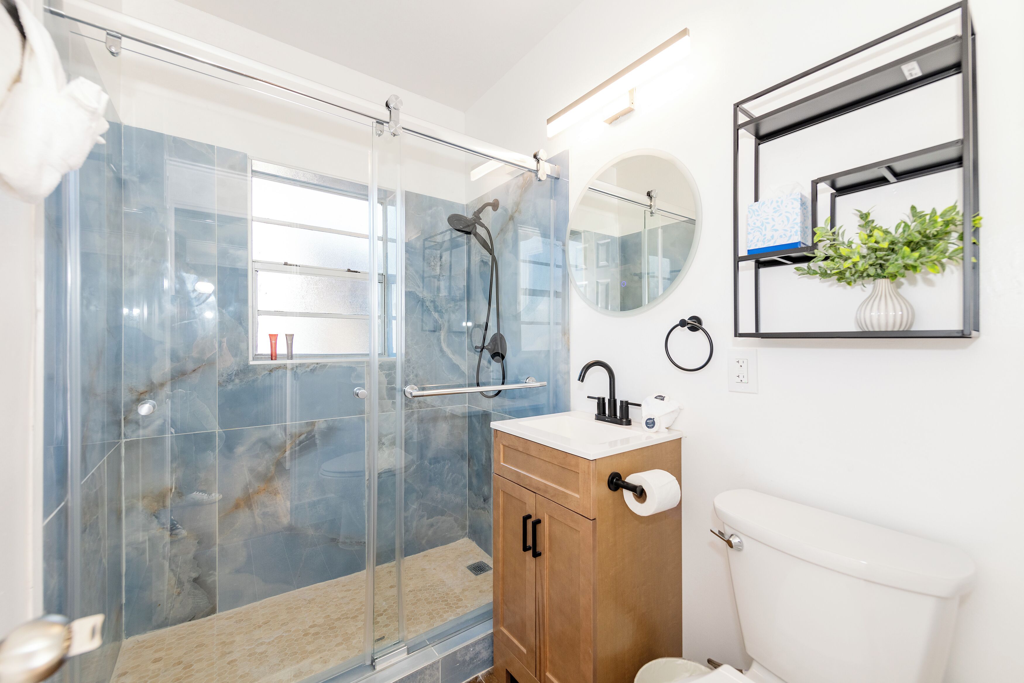 Ein modernes Badezimmer mit einer gläsernen Duschkabine, einem Holzboden, einer Toilette und einem an der Wand befestigten Regal mit einer Pflanze.