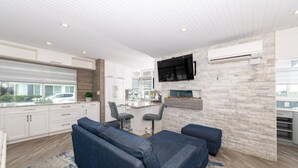 A modern kitchen with white cabinets, a stone backsplash, and a built-in TV. There is a dining area with bar stools and a large window overlooking a parking area. - Tropic Isle Boutique Hotel  (Hollywood)