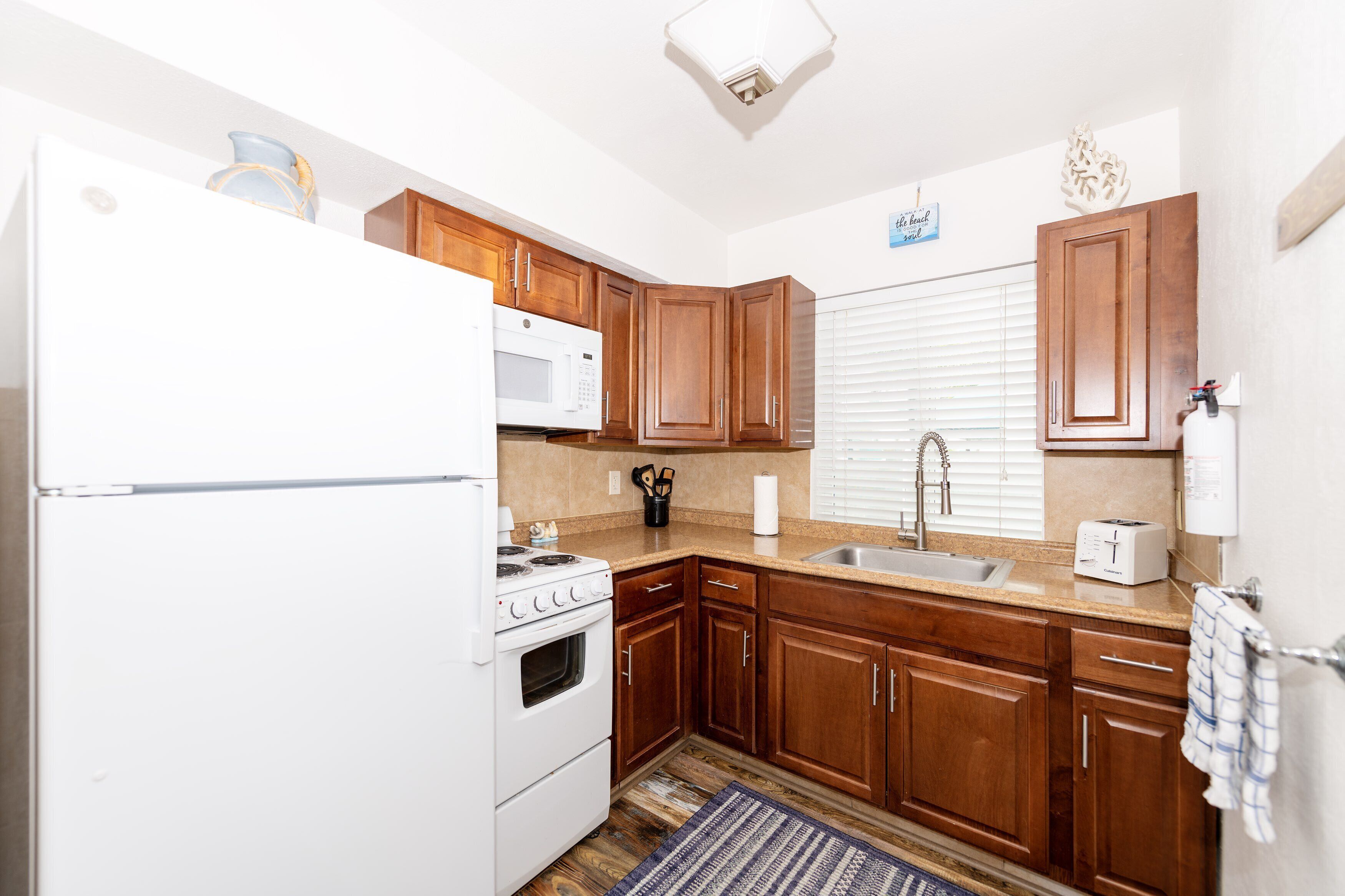 A kitchen with wooden cabinets, a white refrigerator, a microwave, a stove, a sink, and a toaster.