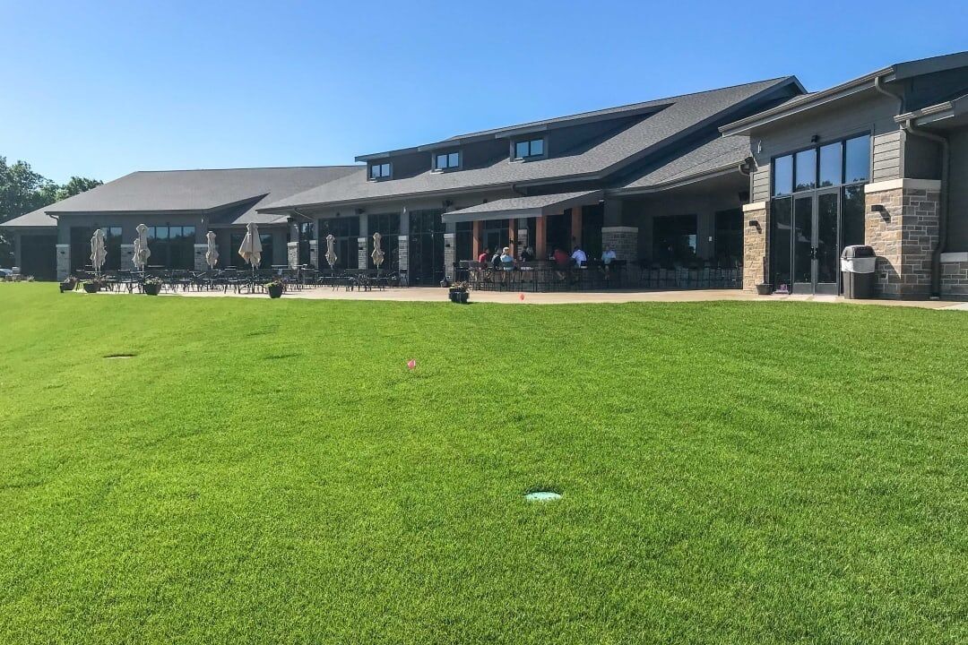A building with a covered patio area, outdoor seating, and a well-maintained lawn.