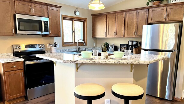 A kitchen with wooden cabinets, stainless steel appliances, granite countertops, and two bar stools. - Lake Arrowhead Retreat with club pools and beaches (Nekoosa)