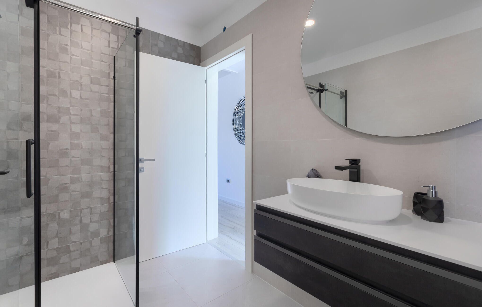 Un bagno moderno con cabina doccia in vetro, un lavandino bianco e uno specchio grande.