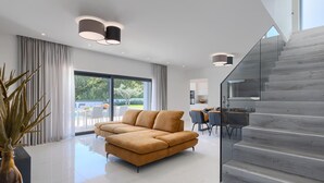 A modern living room with a sectional sofa, a glass staircase, and a dining area with a view of the outdoors. - Stunning home in Barban (Barban)