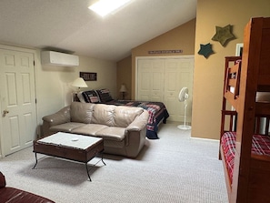 A room with a leather sofa, a small table, a bed with a plaid blanket, a white fan, and a wall sign.