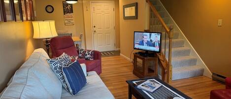 A living room with a sofa, armchair, TV, and a staircase.
