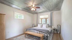 A bedroom with a bed, a bench, a ceiling fan, and a window. - 4K Ranch - 10 acre property & home near Hermann (New Florence)