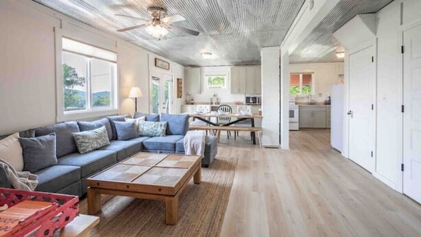 A spacious living area with a sofa, coffee table, and a dining table. A kitchen is visible in the background. - 4K Ranch - 10 acre property & home near Hermann (New Florence)