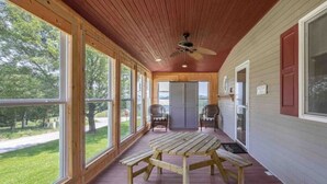 A covered porch with a wooden table and benches, large windows, and a ceiling fan. - 4K Ranch - 10 acre property & home near Hermann (New Florence)