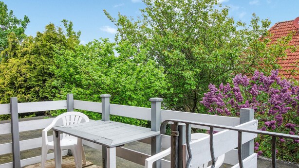 A wooden deck with a white table and chairs, surrounded by lush greenery and purple flowers. - Gorgeous apartment in Otterndorf (Otterndorf)