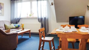 A cozy living room with a sofa, a wooden dining table set for tea, a television, and a window with curtains. - Gorgeous apartment in Otterndorf (Otterndorf)