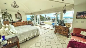 Une chambre spacieuse avec un grand lit, une commode en bois, un canapé rouge et un balcon offrant une vue sur l’océan.