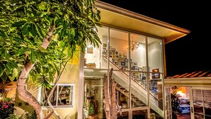 Une maison moderne avec une façade en verre, un escalier menant à l’étage supérieur et une variété de plantes en pot à l’extérieur.