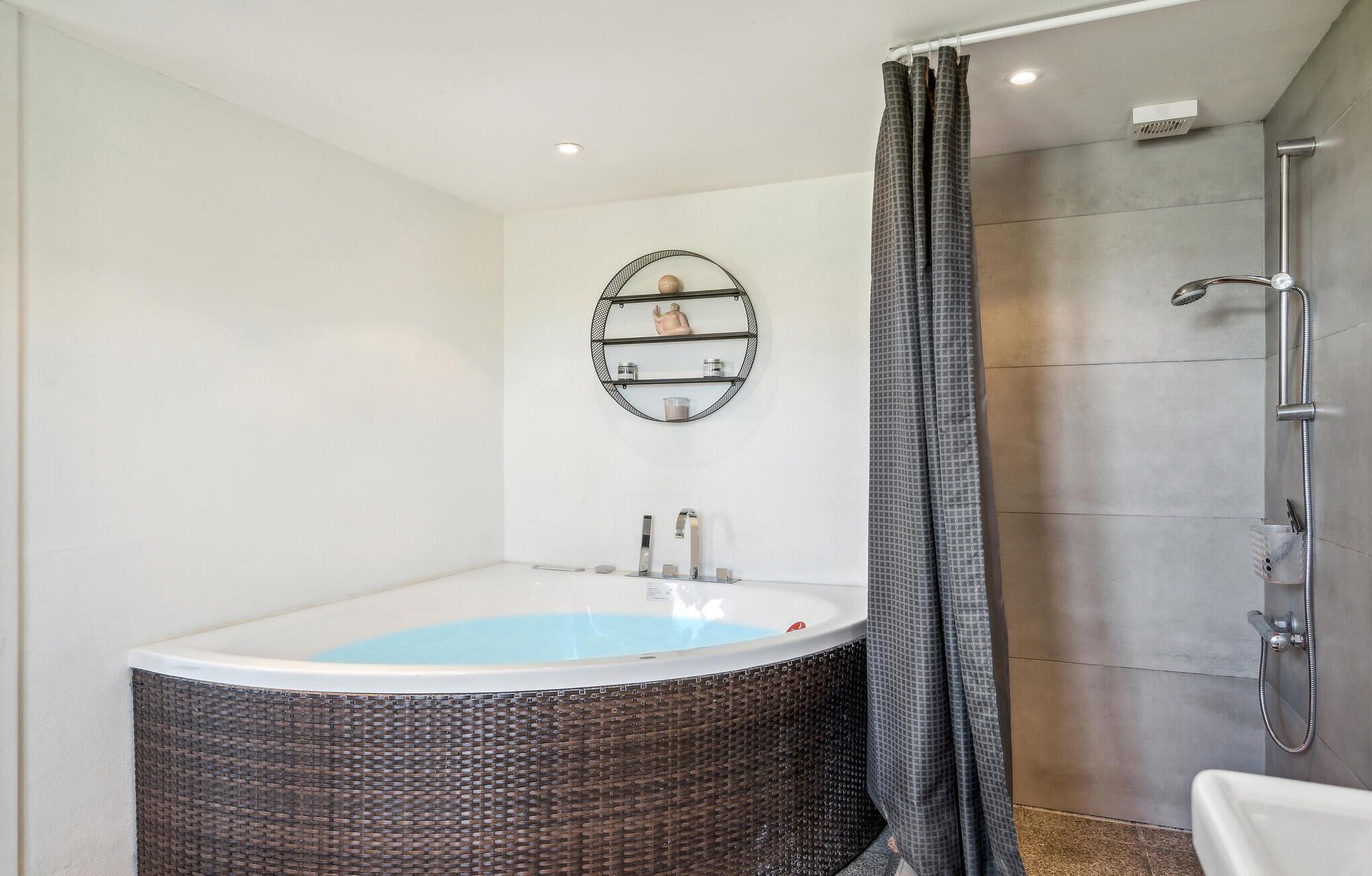 Une salle de bain moderne avec une baignoire sur pieds, une douche et une étagère murale où sont rangés les articles de toilette.