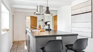 Una cucina moderna con isola centrale, sedie nere, una macchina da caffè e un lampadario.
