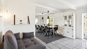 Un soggiorno moderno con un divano grigio, un'area pranzo con un tavolo lungo e sedie, e un mobile bianco con ante in vetro.
