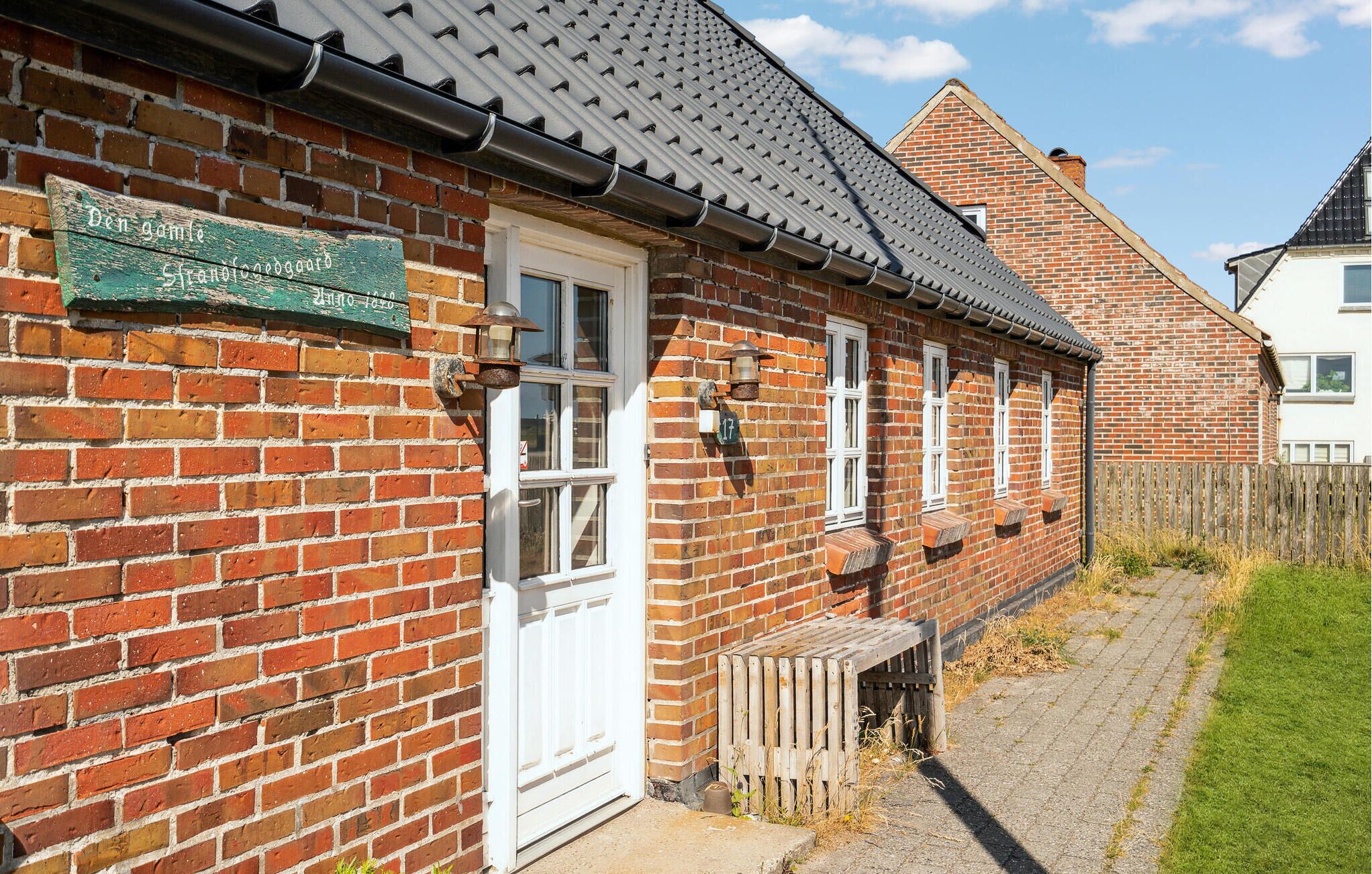 Een bakstenen huis met een witte deur, een klein portaal en een houten hek.
