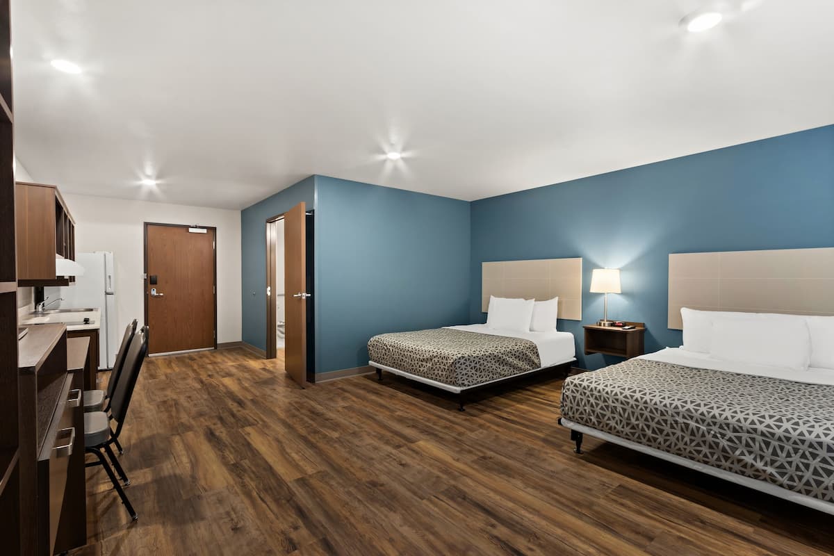 Ett hotellrum med två sängar, ett skrivbord med en stol, ett litet kök och ett badrum.