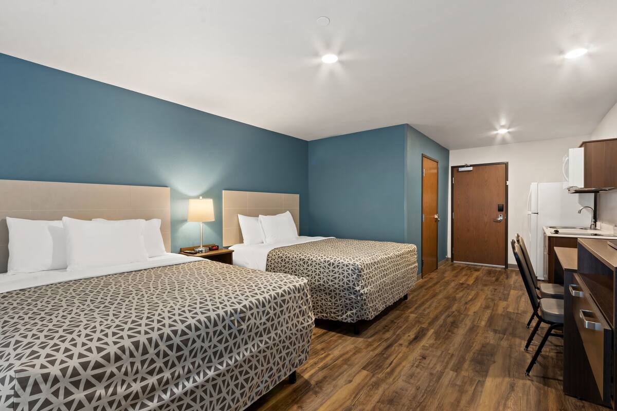 Ett hotellrum med två sängar, ett skrivbord med en stol, ett handfat och en dörr.
