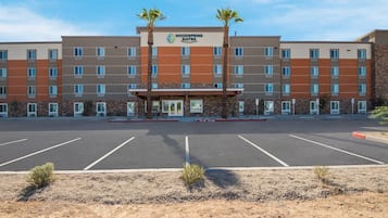 A multi-story hotel with a central entrance, parking lot, and palm trees.