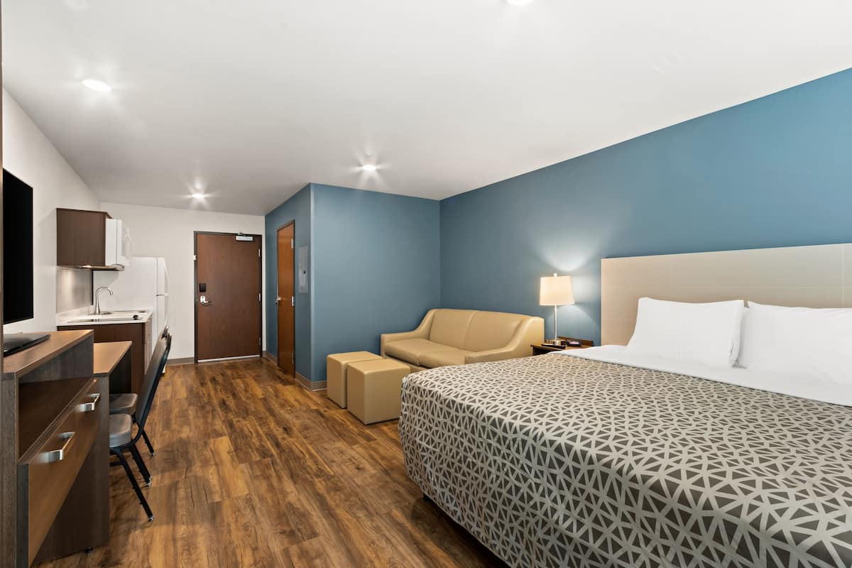 Ett hotellrum med en s äng, ett skrivbord, en stol, en soffa och ett sängbord med en lampa.