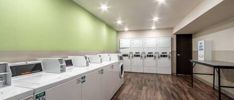 Una sala de lavandería con varias lavadoras y secadoras, suelo de madera y pared verde.