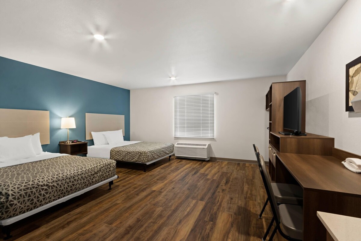 A hotel room with two beds, a desk, a television, and a window with blinds.
