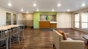 A spacious room with a long table and chairs, a sofa, a small kitchen area, and large windows. - Woodspring Suites Tolleson - Phoenix West (Tolleson)