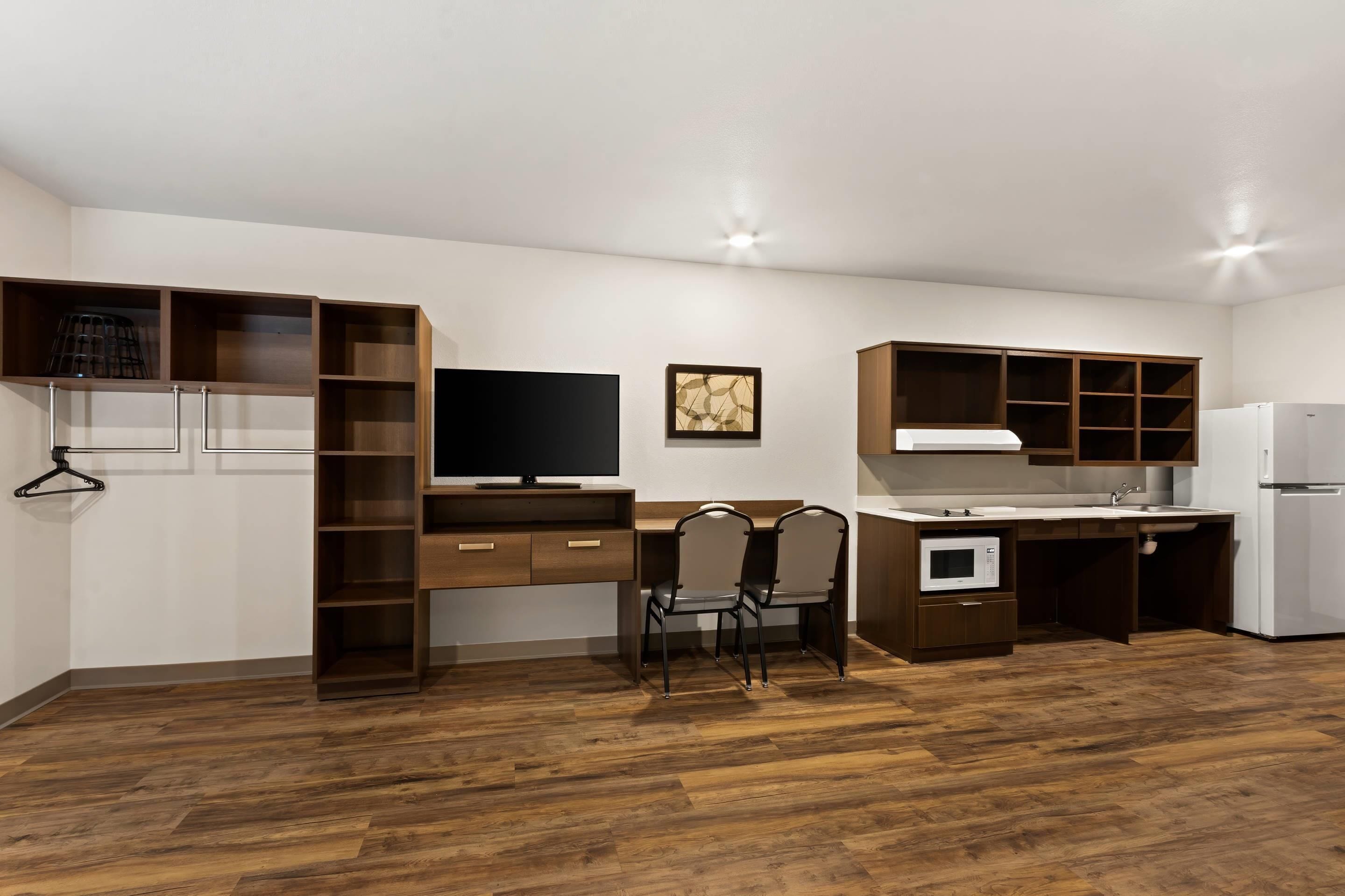 A compact kitchen with wooden cabinets, a built-in microwave, a sink, and a television.