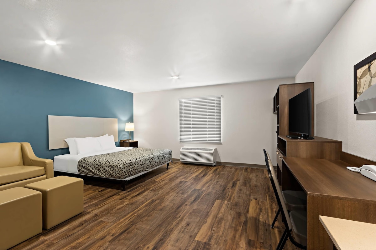 A hotel room with a bed, a desk, a chair, a TV, and a window with blinds.