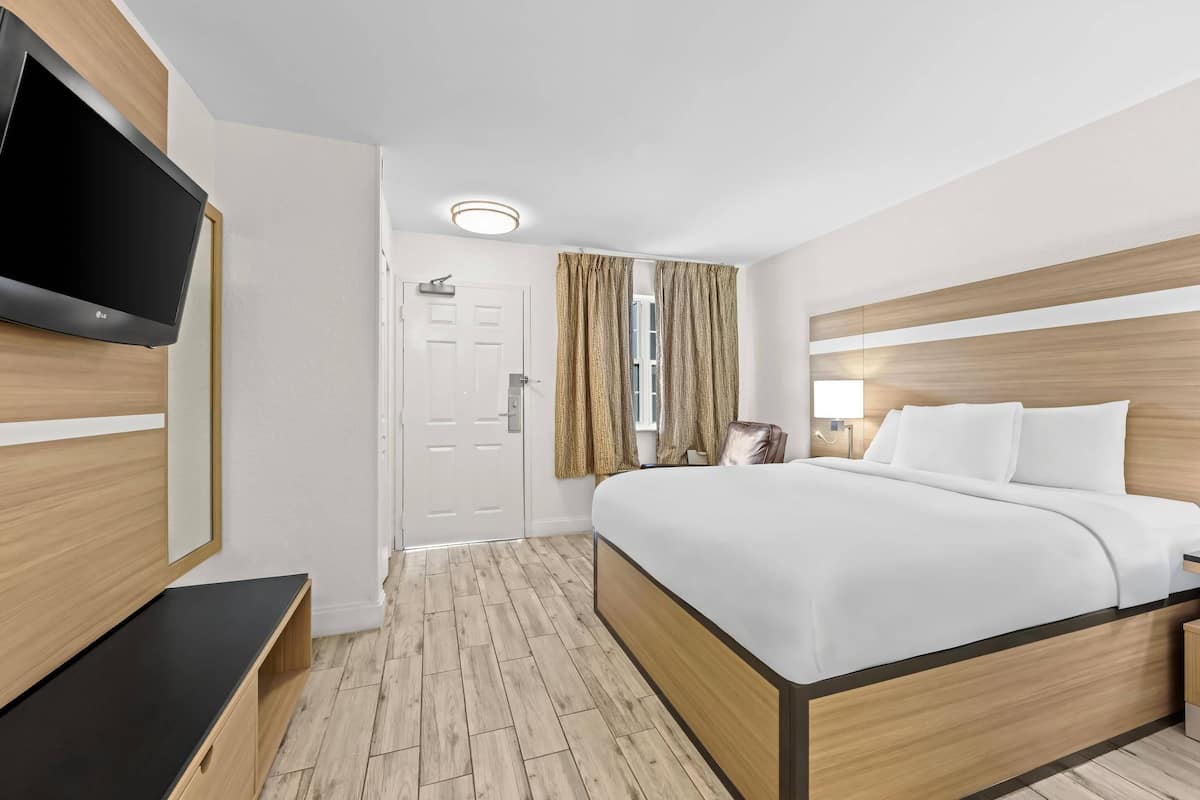 Ein Hotelzimmer mit Bett, Fernseher, Tür und einem Vorhangfenster.