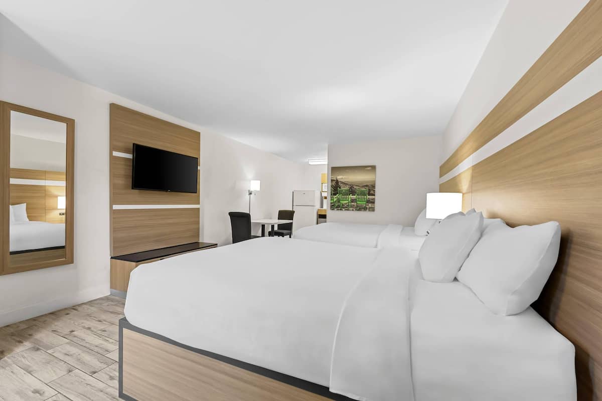 Ein Hotelzimmer mit einem großen Bett, einem Schreibtisch, einem Stuhl, einem Flachbildfernseher und einem Gemälde an der Wand.