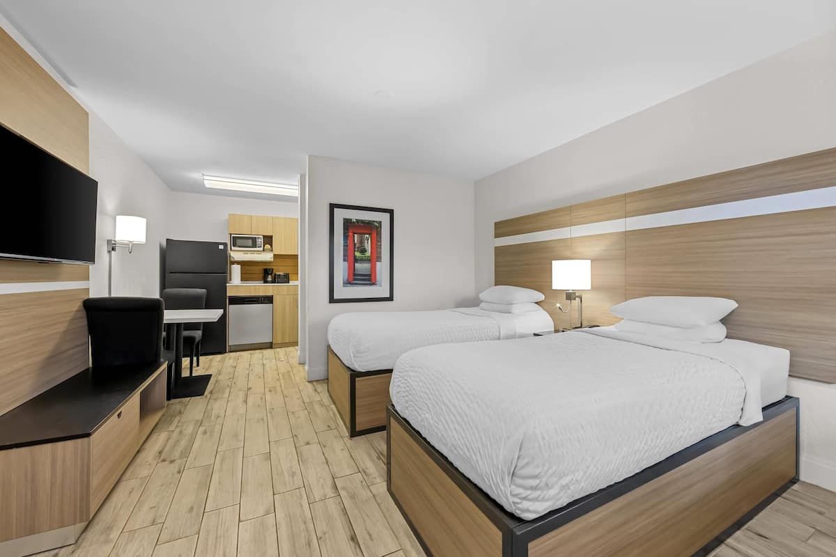 Ein Hotelzimmer mit einem Bett, Nachttischen, einem Schreibtisch, einem Sessel, einem Flachbildfernseher, einer Mikrowelle und einem gerahmten Bild an der Wand.
