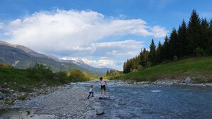 Une rivière à lit rocheux, bordée de verdure et avec des montagnes en arrière-plan.