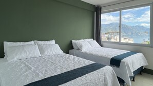 Een kamer met twee bedden, groene wanden en een groot raam met uitzicht op bergen en een wateroppervlak.