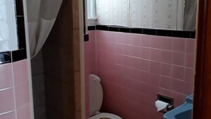 Un baño con paredes de azulejos rosa y negro, un inodoro blanco y un lavabo azul.